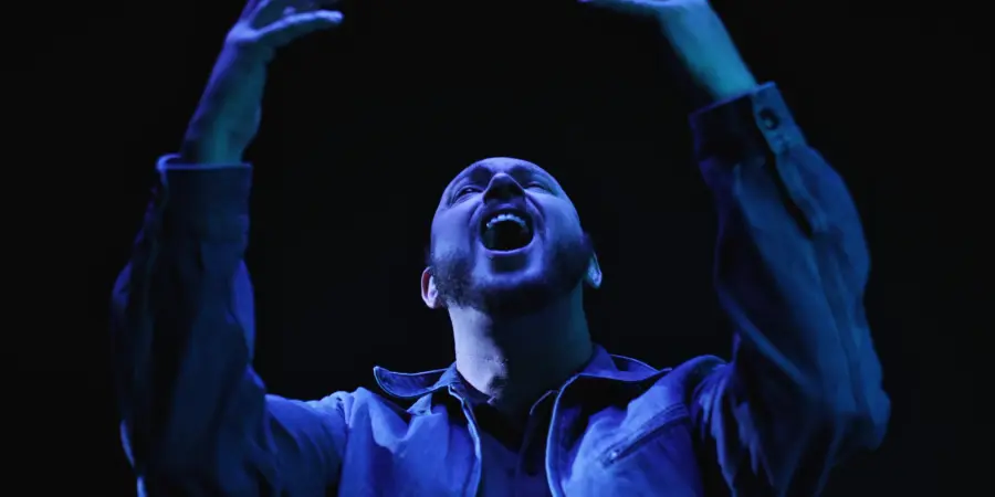 Box of Rules: arms raised overhead under blue light